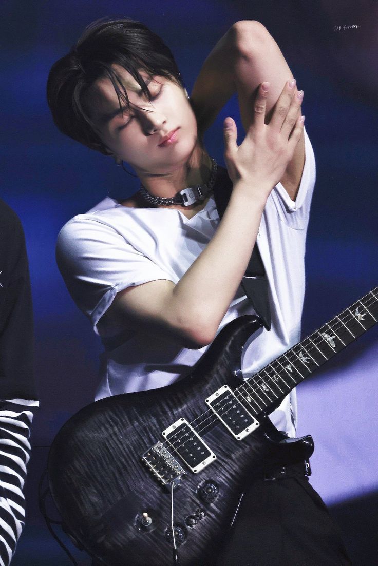 a young man is holding his guitar while wearing a white t - shirt and black pants