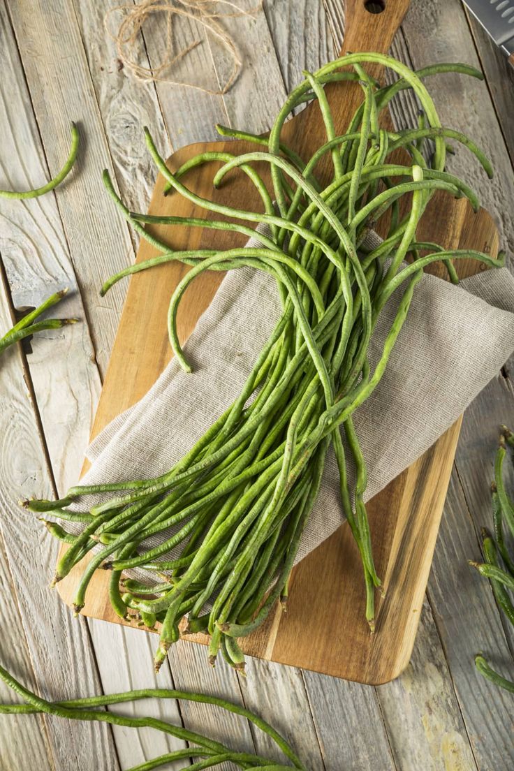 green beans on a wooden cutting board with a knife and napkin next to them,