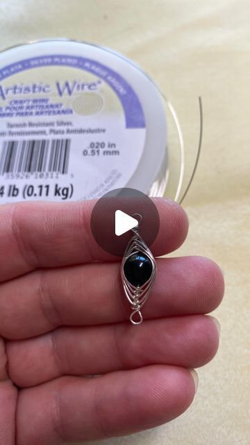 a hand holding a spool of wire with a black bead on it's end