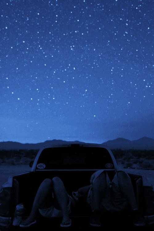 a woman sitting in the back of a pick up truck under a night sky filled with stars