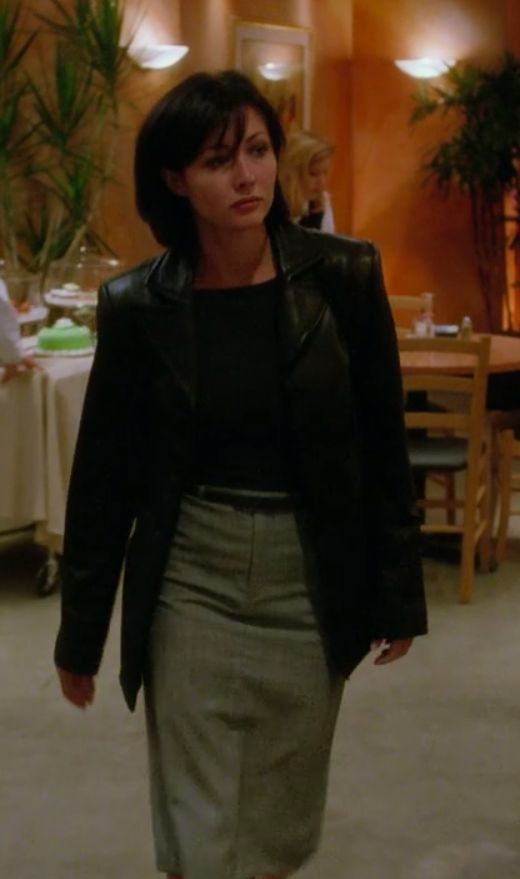 a woman in a black jacket and skirt walking through a room with tables set up for dinner