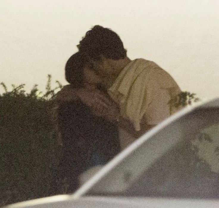 a man and woman kissing in front of a car