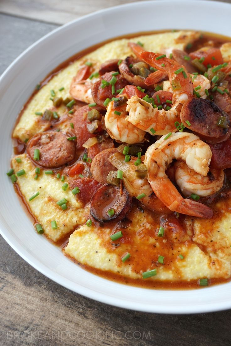 a white plate topped with shrimp and grits covered in sauce on top of a wooden table