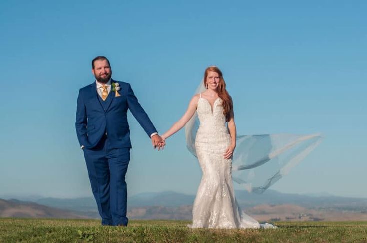 a bride and groom holding hands while standing in a field