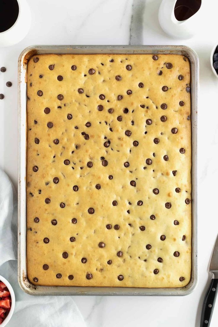 a pan filled with batter and chocolate chips on top of a white table next to bowls of fruit