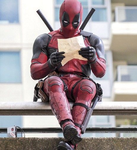 deadpool sitting on a bench reading a piece of paper and holding two baseball bats