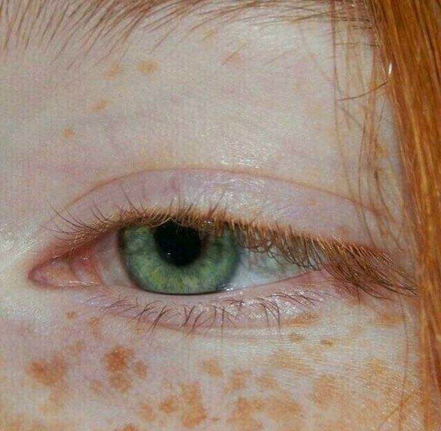 an orange haired woman with freckles on her face looking at the camera, close up