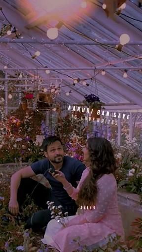 a man sitting next to a woman in a greenhouse filled with plants and flowers on the ground