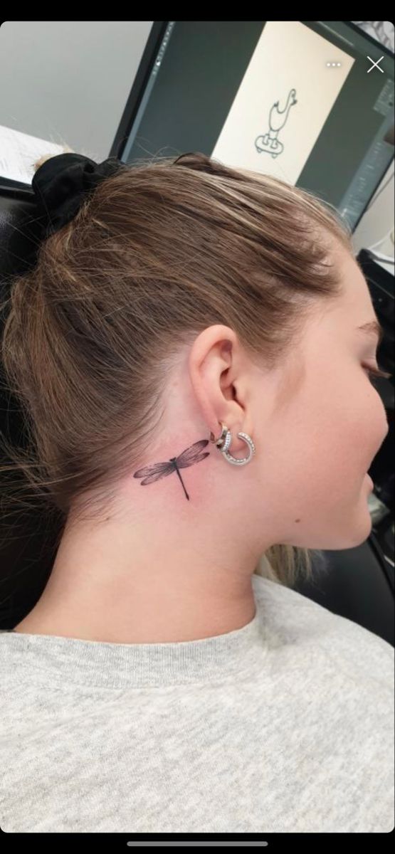 a woman with a tattoo on her neck and behind her ear is looking at the camera