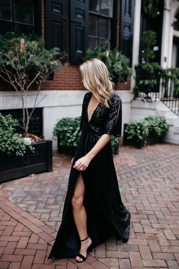 a woman in a black dress is walking down the street with her legs crossed and wearing sandals