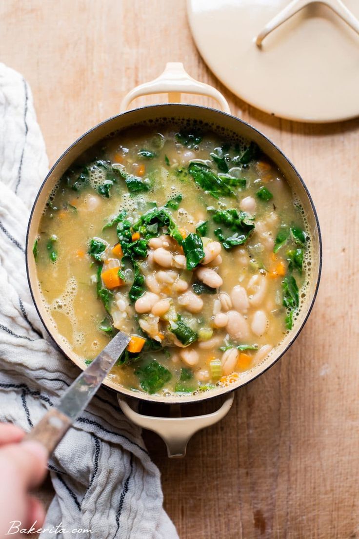 a pot filled with beans and spinach on top of a wooden table next to a spoon