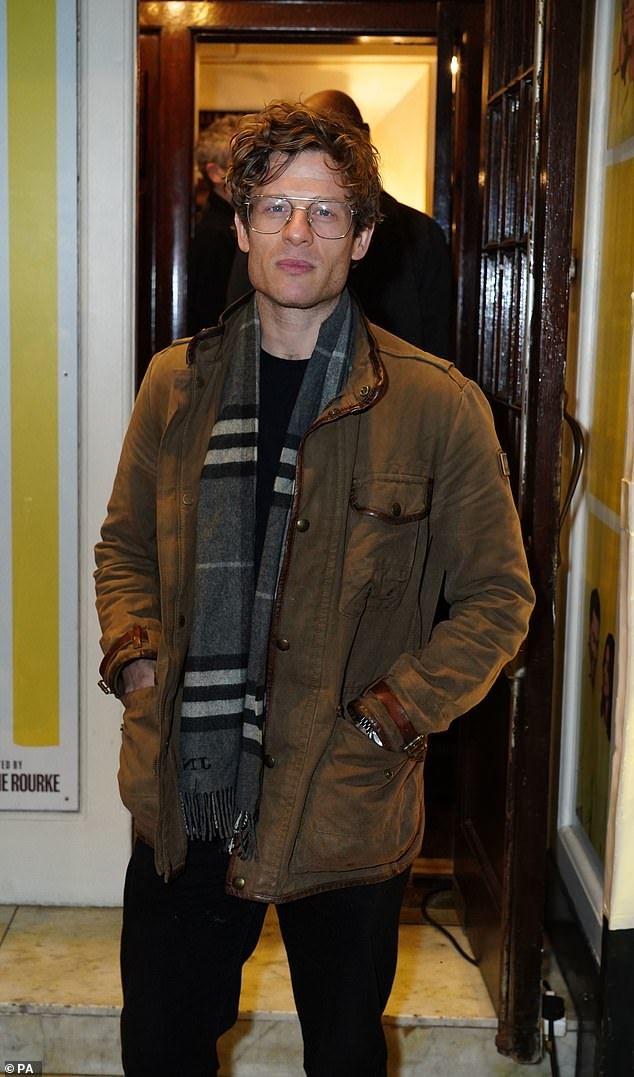 a man standing in front of a door wearing glasses and a scarf around his neck