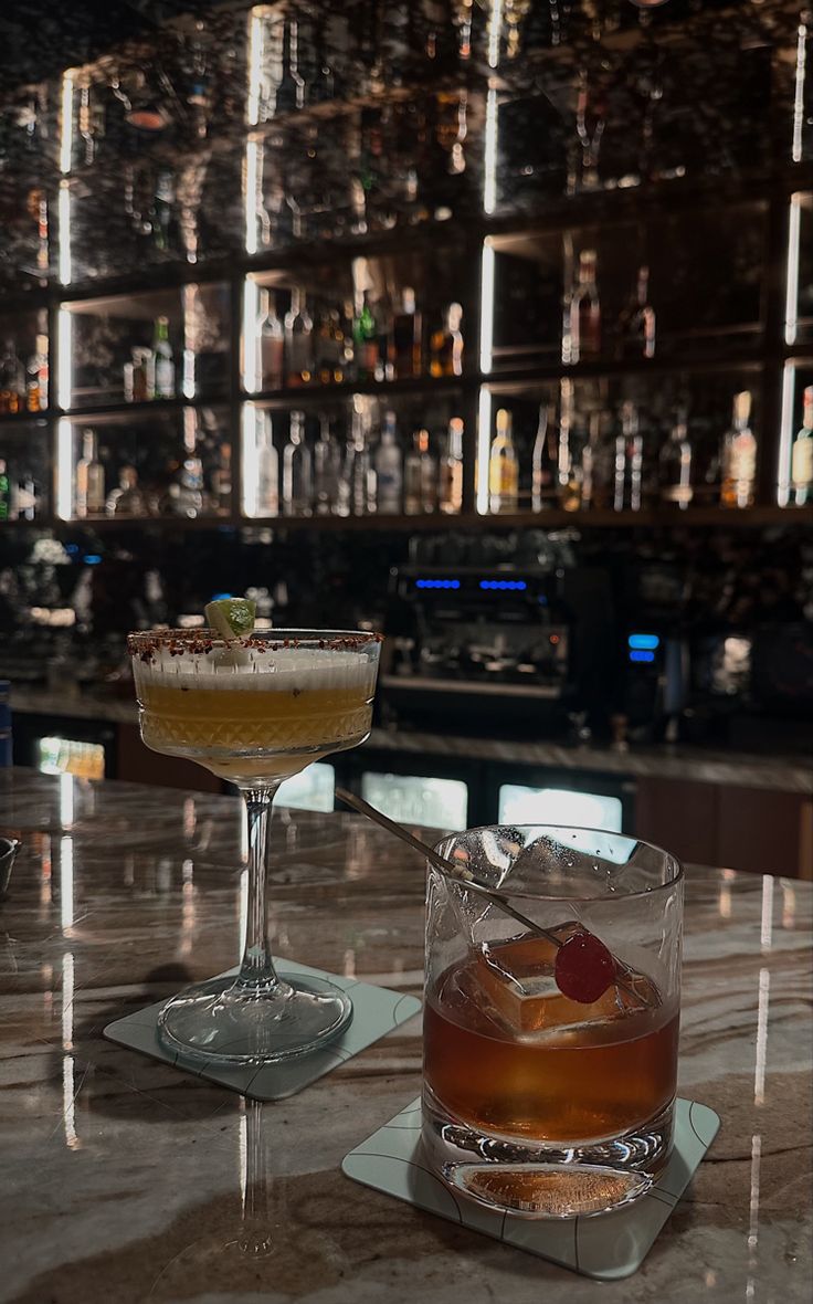 two cocktails sitting on top of a bar next to each other