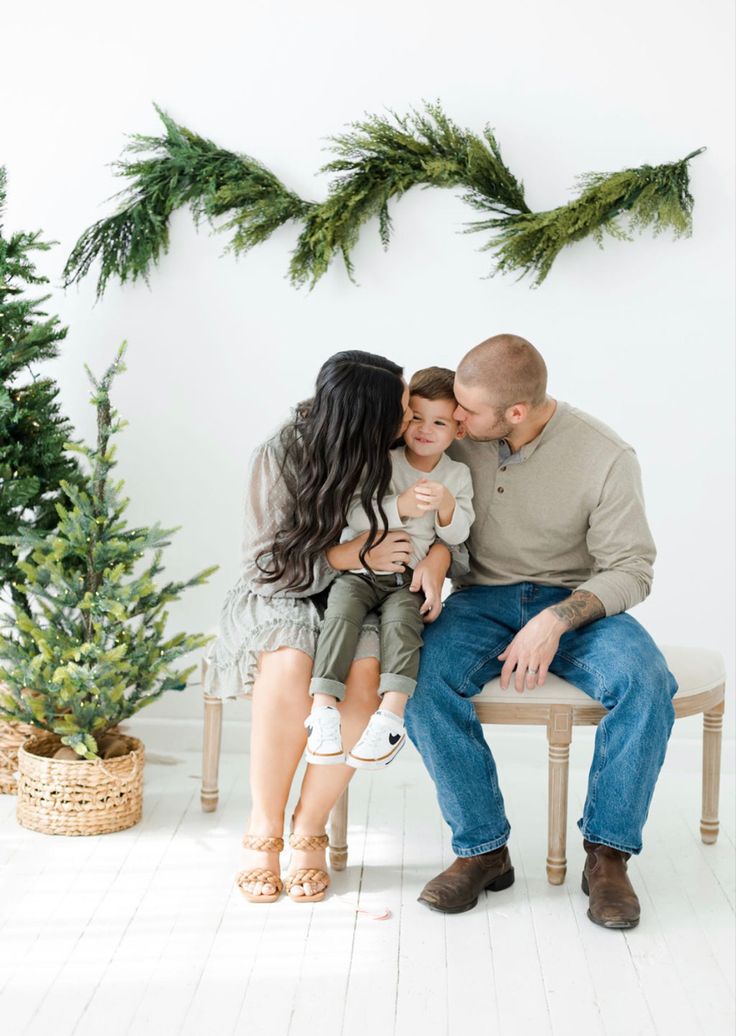 a family sitting on a bench in front of christmas trees and garlands with their arms around each other