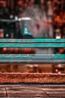 a green bench sitting in front of a store window with the reflection of another building behind it