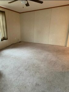 an empty living room with carpeted floor and ceiling fan in the corner, next to a window