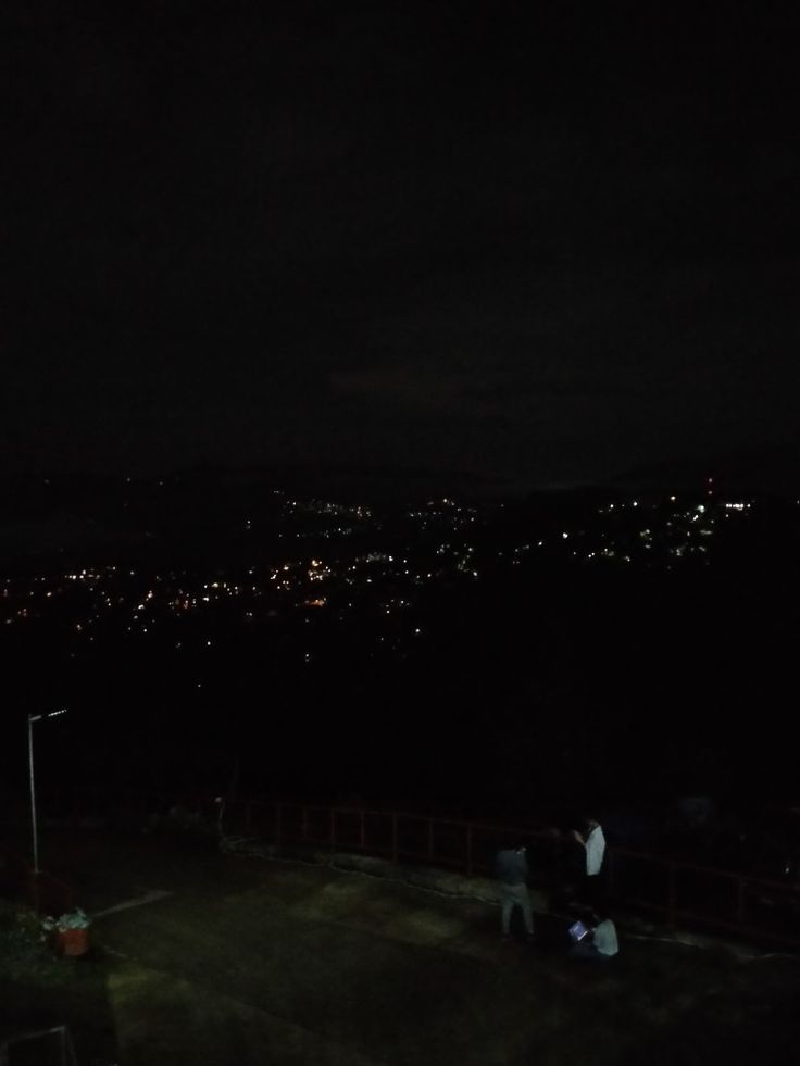 two people standing on top of a hill at night with the city lights in the background