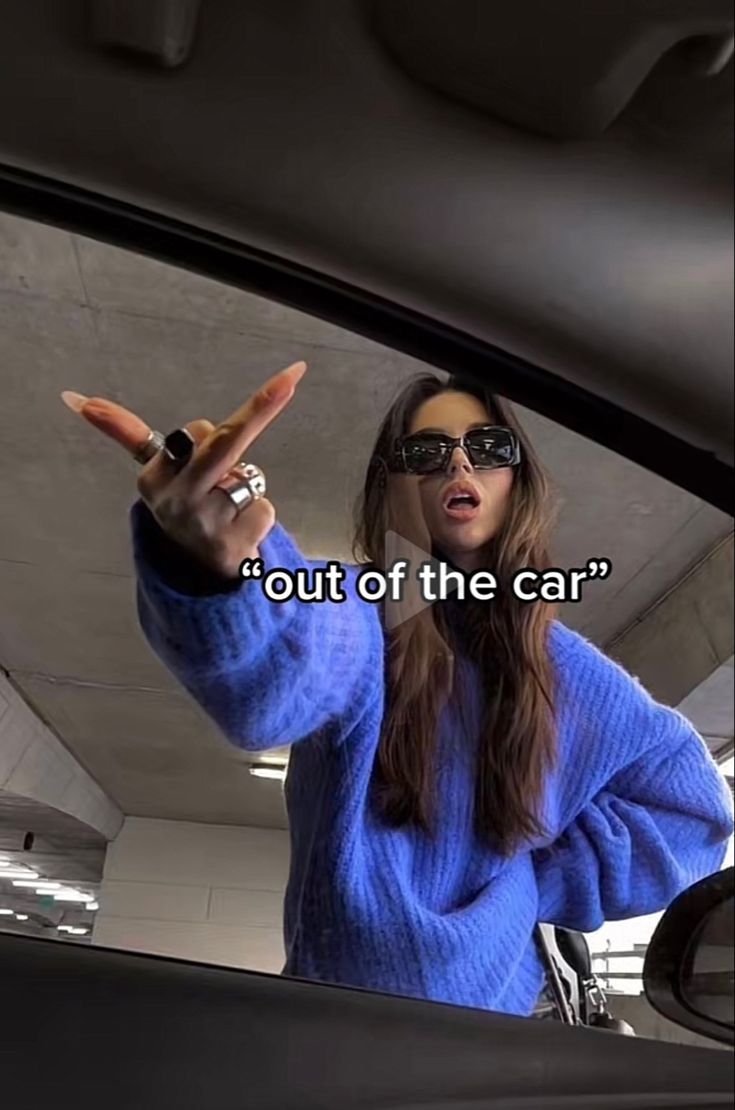 a woman in blue sweater holding up her hand with the words out of the car