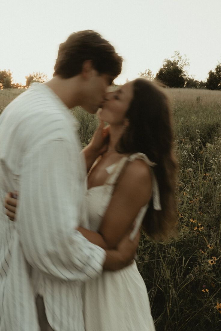 a man and woman are kissing in a field with tall grass on the other side