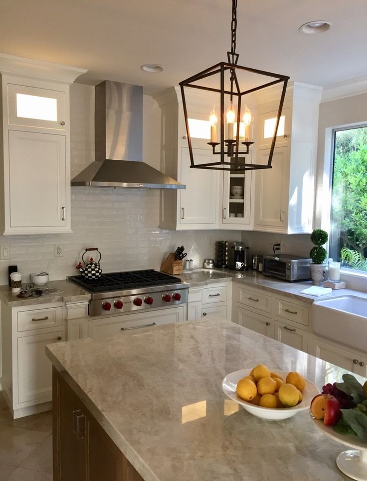 a large kitchen with white cabinets and marble counter tops, an island in the middle has two bowls of fruit on it