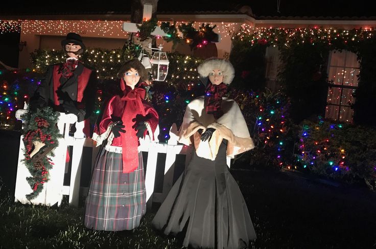 three mannequins dressed up in christmas attire standing next to a white picket fence