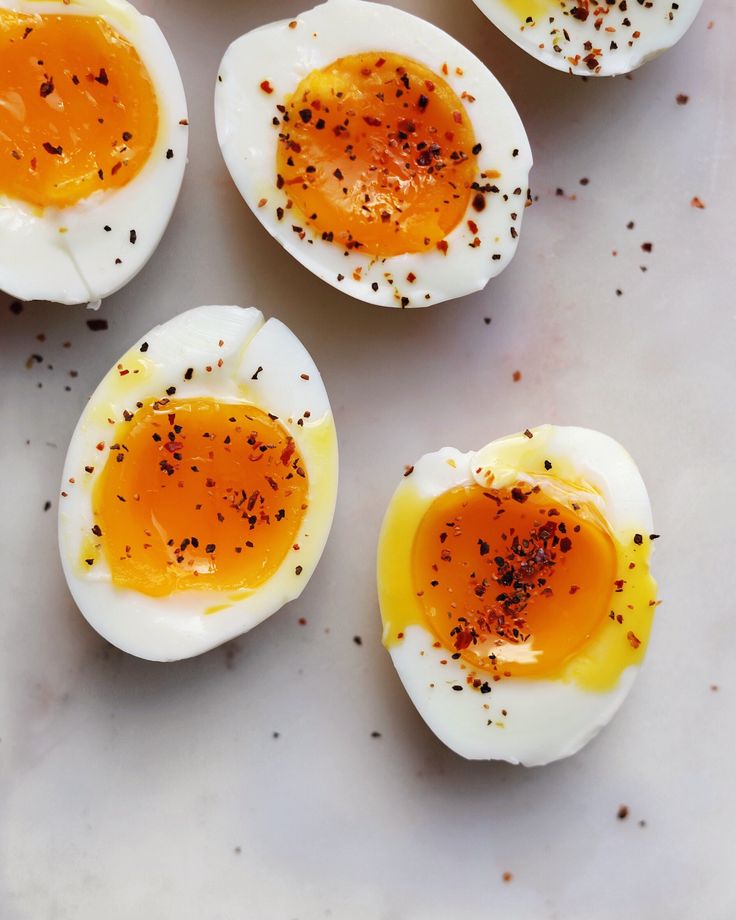 four hard boiled eggs on a white surface with seasoning sprinkled around them