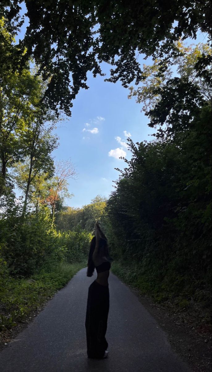 a woman standing on the side of a road with her arms up in the air