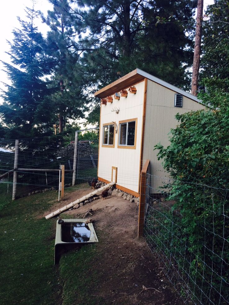 a tiny house built into the side of a fenced in area with grass and trees