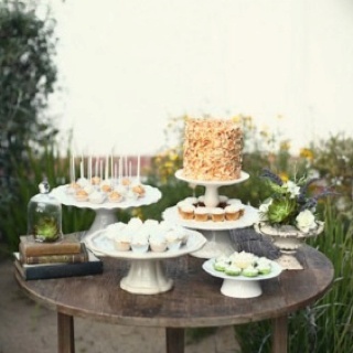 a table topped with cakes and desserts on top of wooden tables next to flowers