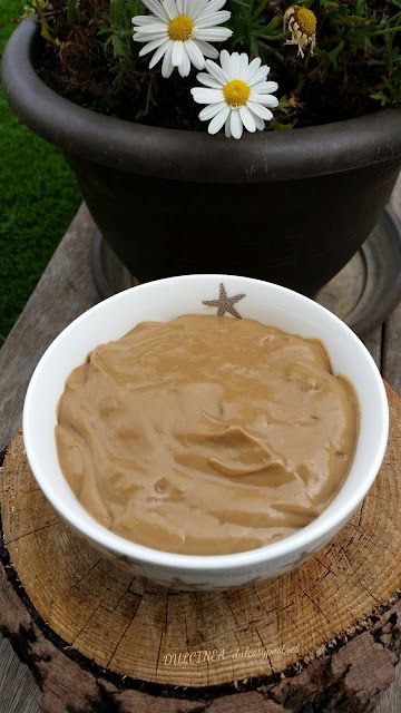 a bowl of peanut butter sitting on top of a wooden table next to a potted plant