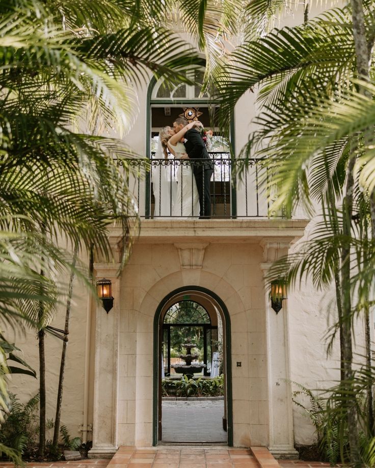 a bride and groom standing on their balcony in front of a building with palm trees