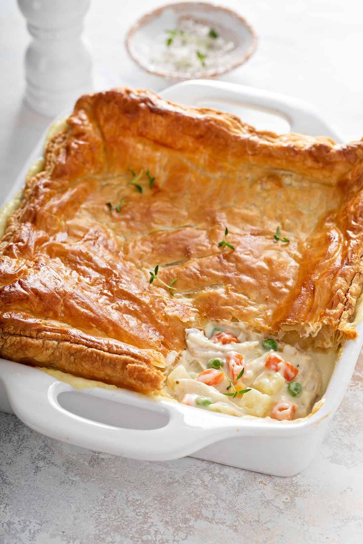 a casserole dish with meat and vegetables in it sitting on a white table