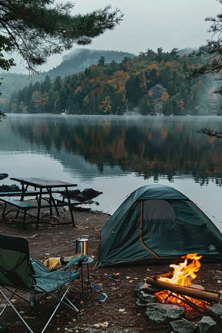 a tent is set up next to a campfire on the shore of a lake