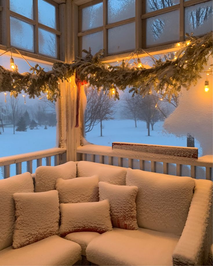 a couch covered in snow next to a window with christmas lights hanging from the ceiling