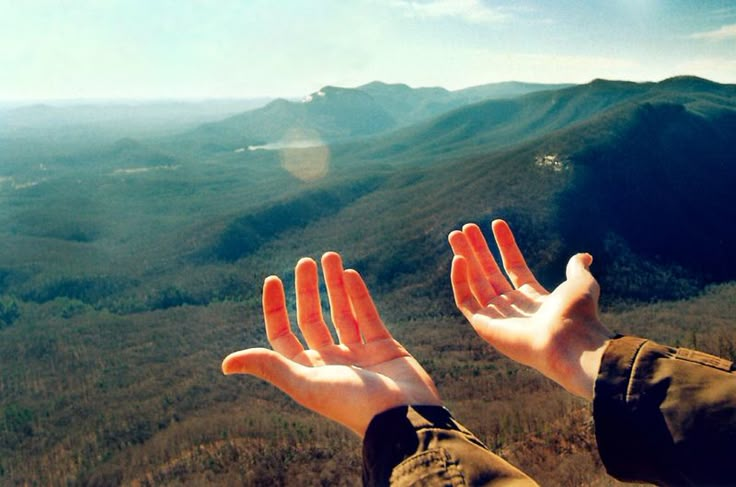 someone is holding their hands up in the air with mountains and hills in the background