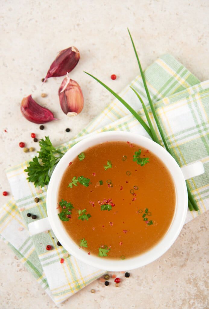 a white bowl filled with soup sitting on top of a table next to garlic and herbs