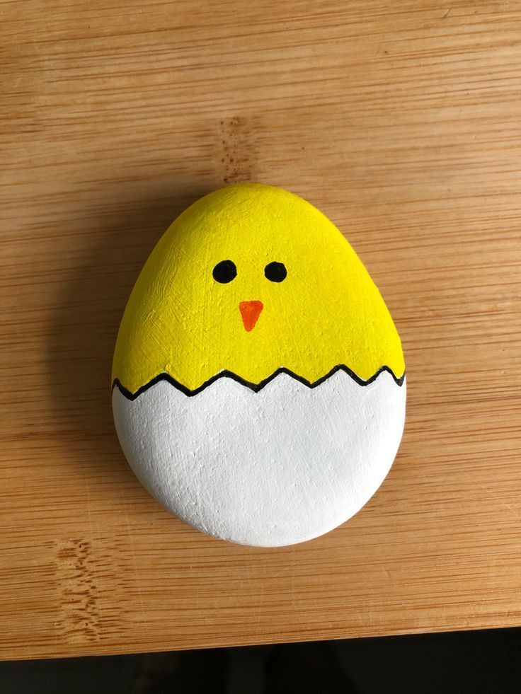 a painted rock with a yellow chick in it's egg shell on a wooden surface