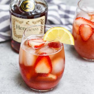 a close up of a drink in a glass with strawberries and lemon wedges