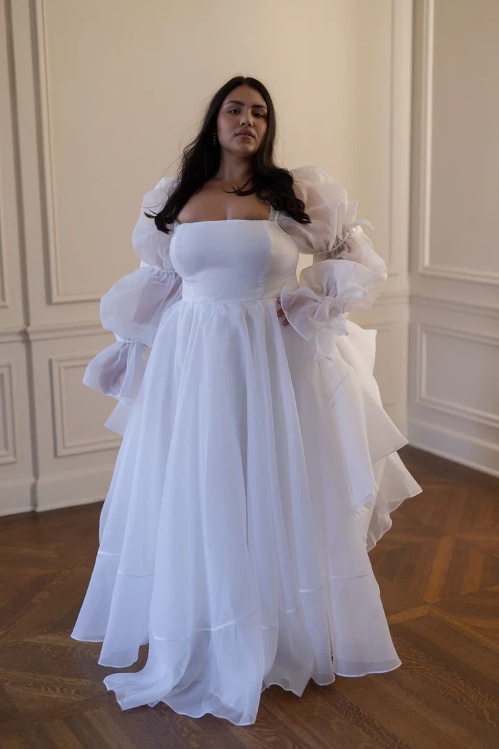 a woman wearing a white dress standing in a room with wood flooring and walls