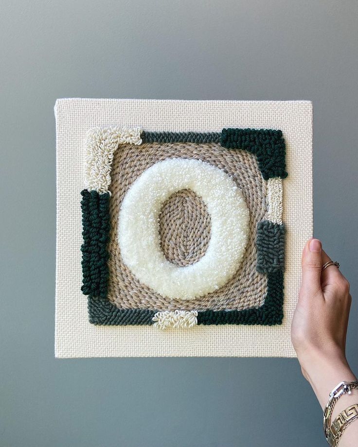 someone is holding up a knitted rug with a circle on the bottom and green trim around it