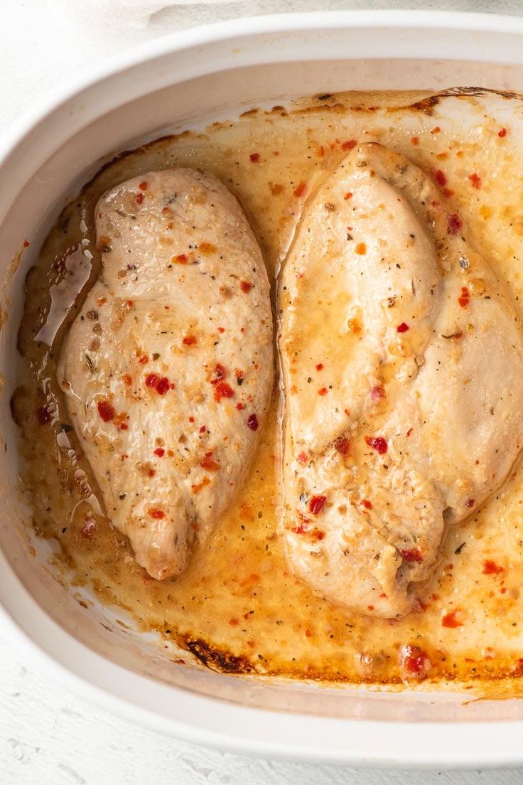 two pieces of chicken in a white casserole dish with sauce on the side