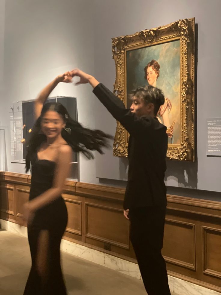 a man and woman dancing in an art gallery with paintings on the wall behind them