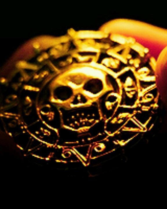 a close up of a person's hand holding a gold coin with skulls on it