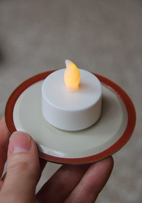 a person holding a small white candle on a plate with a red rim around it