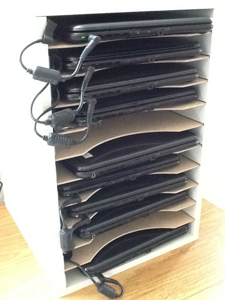 a stack of black laptops sitting on top of a wooden floor next to a white wall