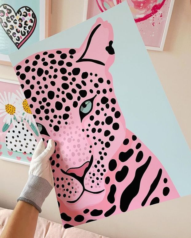 a person holding up a paper cut out of a pink and black leopard head on a wall