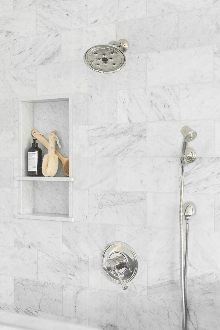 there is a shower head and some shelves on the wall in this white marble bathroom