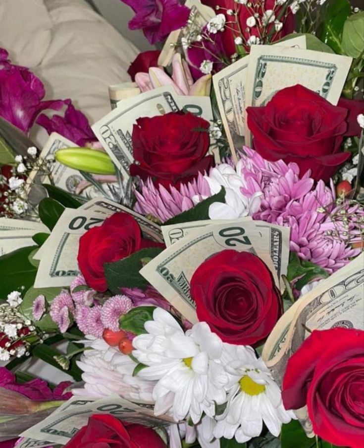 a bouquet of flowers and money sitting on top of a bed covered in red roses