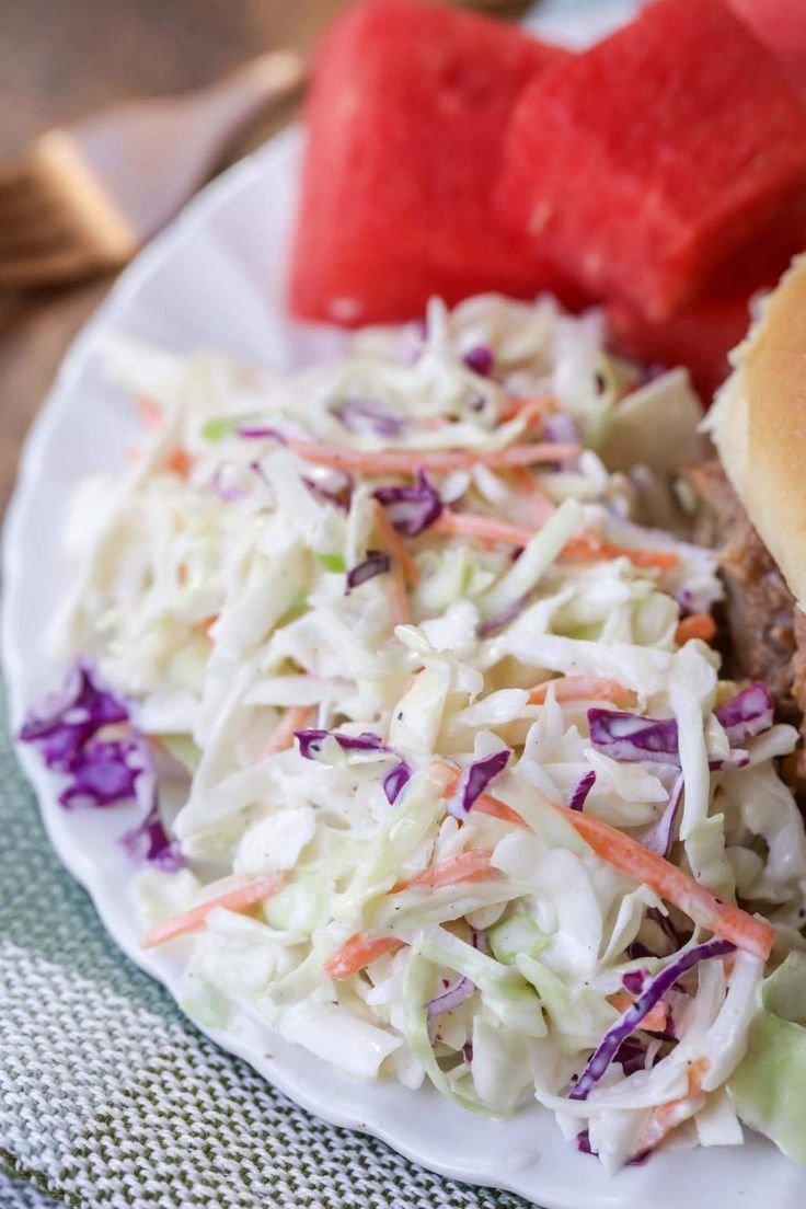 a hamburger and coleslaw on a plate with watermelon