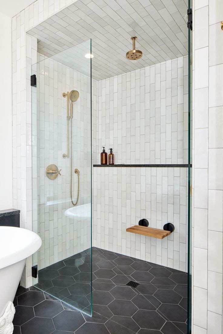 a bathroom with a glass shower door and black floor tiles on the walls, along with a white bathtub